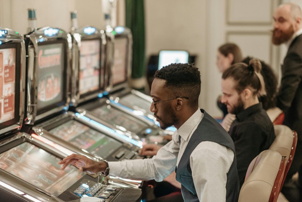 A man sits alone at a slot machine in a dimly lit casino, eyes fixated on the screen, illustrating the loneliness and compulsion of active addiction through gambling.